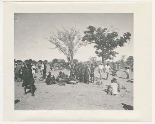 "1950 '400 Series' / 87 B/W prints (some duplicates) / Ovamboland": Group of people sitting and standing, with baskets of grain on the ground near them (print is a cropped image)