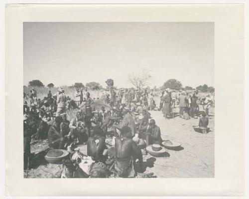 "1950 '400 Series' / 87 B/W prints (some duplicates) / Ovamboland": Group of people sitting and standing, with baskets of grain on the ground near them (print is a cropped image)