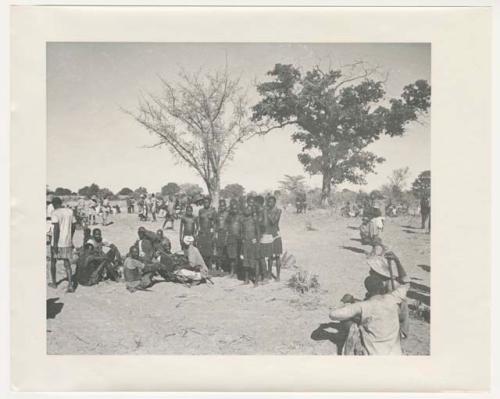 "1950 '400 Series' / 87 B/W prints (some duplicates) / Ovamboland": Group of people sitting and standing, with baskets of grain on the ground near them (print is a cropped image)