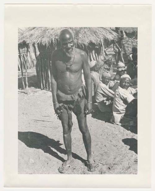 "1950 '400 Series' / 87 B/W prints (some duplicates) / Ovamboland": Man standing next to a group of people sitting (print is a cropped image)