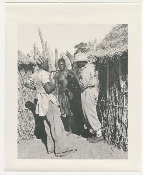 "1950 '400 Series' / 87 B/W prints (some duplicates) / Ovamboland": People standing between huts (print is a cropped image)