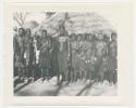 "1950 '400 Series' / 87 B/W prints (some duplicates) / Ovamboland": Group of women standing in a line, with thatched roof in background (print is a cropped image)