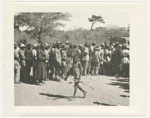 "1950 '400 Series' / 87 B/W prints (some duplicates) / Ovamboland": Boy walking in front of a group of people standing in line (print is a cropped image)