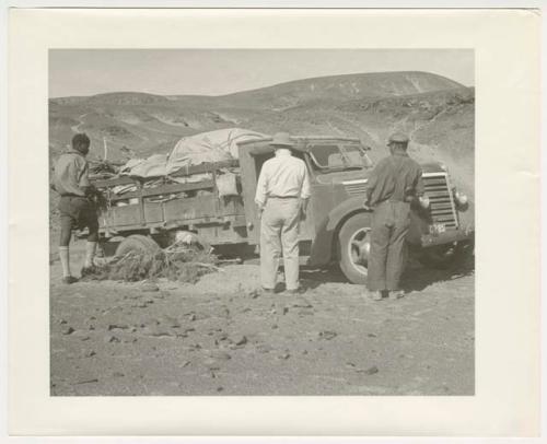 "1950's 400 series": Expedition members standing and looking at the truck, with brush under the wheels, at the crest of a hill (print is a cropped image)