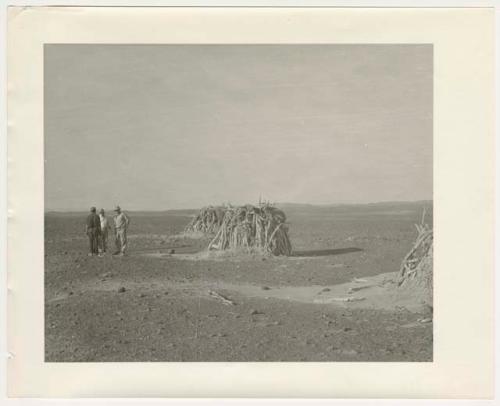 "1950's 400 series": Three men standing near huts (print is a cropped image)