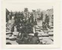 "1950 '400 Series' / 87 B/W prints (some duplicates) / Ovamboland": Group of people sitting and standing next to baskets of grain on ground (print is a cropped image)