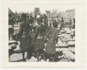 "1950 '400 Series' / 87 B/W prints (some duplicates) / Ovamboland": Group of people sitting and standing next to baskets of grain on ground  (print is a cropped image)