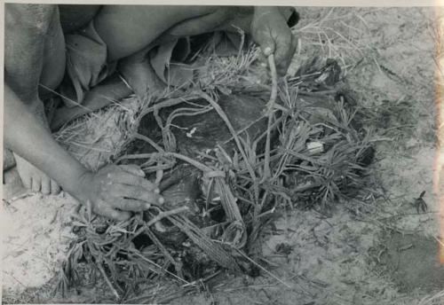 [No folder title]: Close-up of !Gai's hands tying up a carrying net









