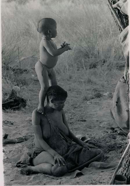 [No folder title]: N!whakwe standing on his mother Tsekue's shoulder to look over the grass to see what was making noise








