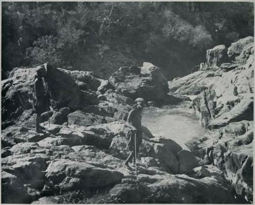 "1950 '400 Series' / 41 prints": Two men walking on rocks at the top of Ruacana Falls (print is a cropped image)