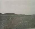 "1950 400 series  40 prints / Kaokoveld": Person sitting, with buttes in background (print is a cropped image)