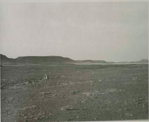 "1950 400 series  40 prints / Kaokoveld": Person sitting, with buttes in background (print is a cropped image)