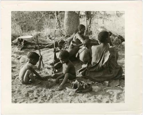 [No folder title]: !Ungka Norna and Bau playing with digging sticks next to a group of people sitting (print is a cropped image)