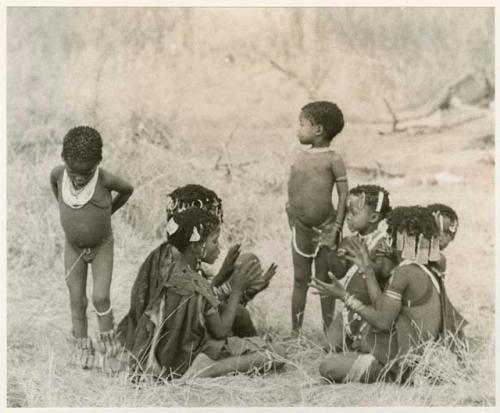 [No folder title]: Girls clapping and singing in a circle, with a little boy dancing (print is a cropped image)