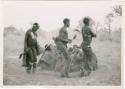 [No folder title]: Three men, including /Gunda and ≠Gao, dancing around a group of seated women singing; medicine man leaning over "Gao Medicine" far back behind (print is a cropped image)