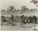 [No folder title]: Women and children sitting in the shade while Elizabeth Marshall Thomas holds a child, distant view (print is a cropped image)