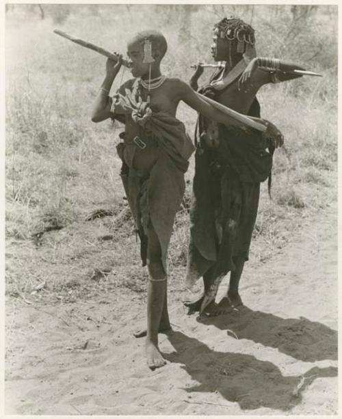 [No folder title]: Two girls with their arms over their digging sticks which are across their shoulders (print is a cropped image)