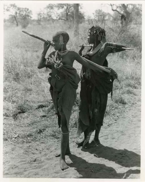 [No folder title]: Two girls with their arms over their digging sticks which are across their shoulders (print is a cropped image)