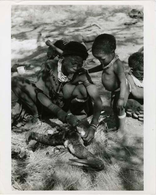 [No folder title]: Di!ai cutting a wildebeest head with Debe standing beside her and other unidentified people (print is a cropped image)