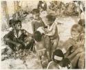 [No folder title]: /Gaishay and an unidentified, young woman helping Debe drink from an ostrich eggshell while Bau watches; other unidentified women and children sitting in the werft (print is a cropped image)