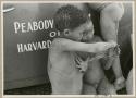 [No folder title]: Two boys making a "cat's cradle" in front of the expedition truck (print is a cropped image)