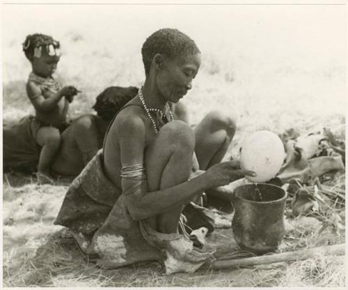 [No folder title]: /Naoka, first wife of "Gao Medicine," emptying an ostrich egg into a pot, with child sitting on somebody's back behind her (print is a cropped image)