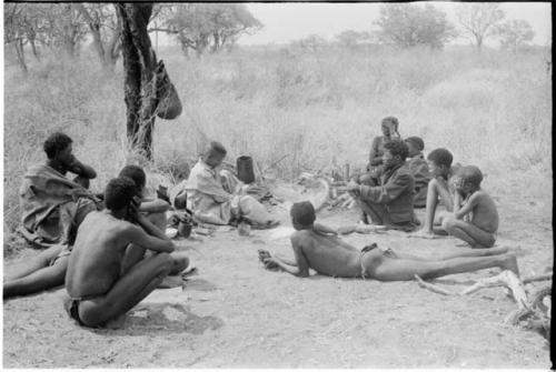 "/Qui Hunter" and ≠Toma sitting with other Ju/'hoansi, seen from a distance