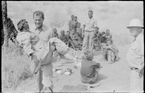 William Donnellan carrying "/Qui Hunter" to the truck with Laurence Marshall, Elizabeth Marshall Thomas, Kernel Ledimo, and other Ju/'hoansi present