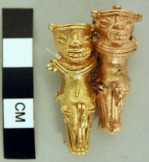 Pin made from two half-human/half-crocodile (?) figures, each of a different col