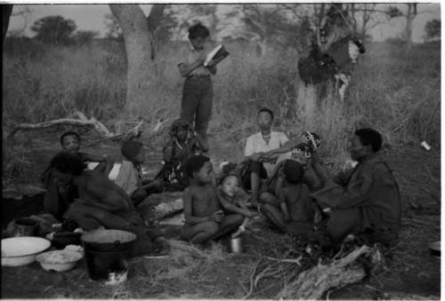 Group of Ju/'hoansi and Elizabeth Marshall Thomas taking notes in the background