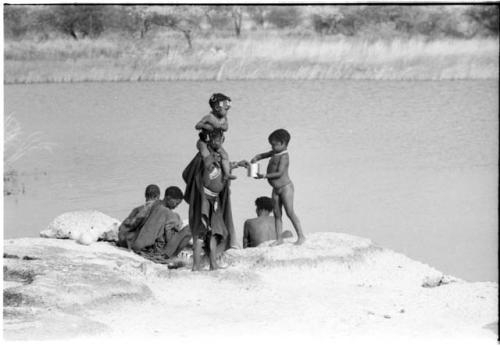 Boy handing a can to a woman at the water, with other people around