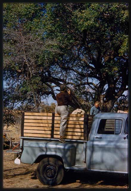 Lorna Marshall taking a photo standing on a truck, with Foppe Hoogheimstra behind her