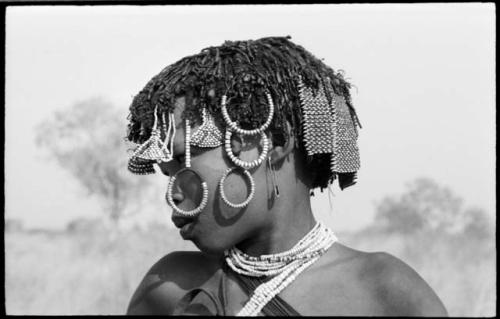 N!ai showing her head ornaments; the triangular ones hanging over her forehead are said to be female, whereas the rectangular ones at the back of her head are said to be male