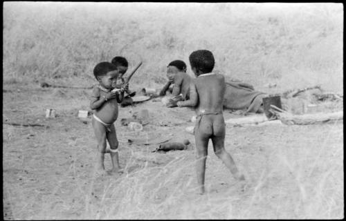 Debe (Di!ai's son) and two other children eating mealies from the spoon, with !U lying in background