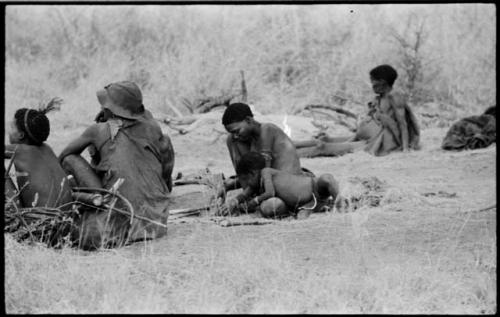 Bau leaning over her mother //Khuga's knee, with two men sitting before them