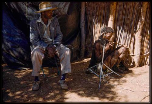 Woman sitting and playing a musical bow, with Kernel Ledimo sitting next to her