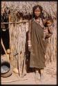 Woman standing and holding a child in front of a hut