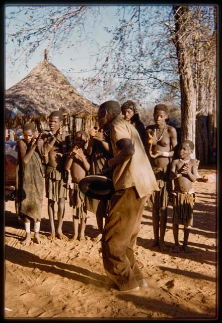 Man dancing at the beginning of a dance, with women and children standing and clapping