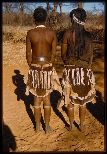 Two women standing with their backs to the camera, showing their aprons