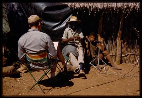 Woman sitting next to a microphone, with Kernel Ledimo and Nicholas England sitting near her