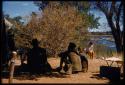 Group of people sitting in the shade, view from behind, with Deborah Marshall sitting in the background sketching