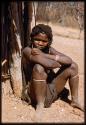 Girl sitting next to a hut, close-up showing her scarification