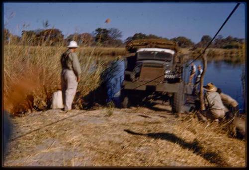 Men unloading the expedition GMC from the pont (ferry) at Bagani, with Laurence Marshall watching