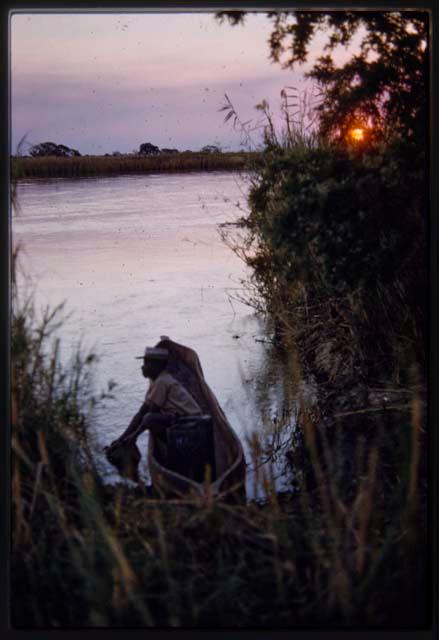 Man sitting in a mokoro (makoro) boat on river at sunset