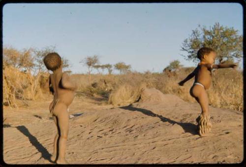 Children, Dancing: Two little boys dancing on a termite mound, one with dance rattles