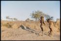 Children, Dancing: Two little boys dancing on an anthill, one with dance rattles