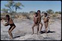 Children, Dancing: Group of boys and girls dancing near a waterhole, with a boy playing a //guashi