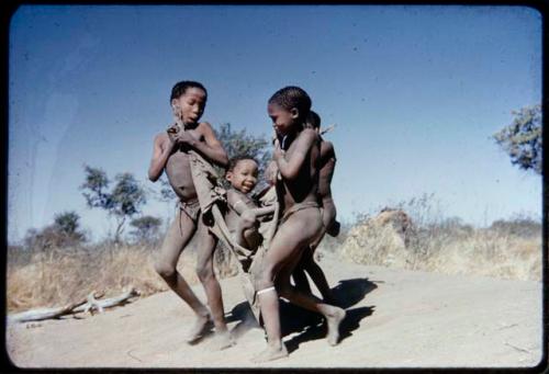 Children, Fathers and sons: Tsamgao (son of ≠Toma) and ≠Gau (son of Gau) carrying "Little ≠Gao" in a kaross, playing "the airplane game"