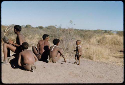 Children, Fathers and sons: Group of boys sitting on a termite mound, with "≠Gao Lame" playing a //guashi and /Gaishay (son of "Gao Medicine" and Di!ai) dancing