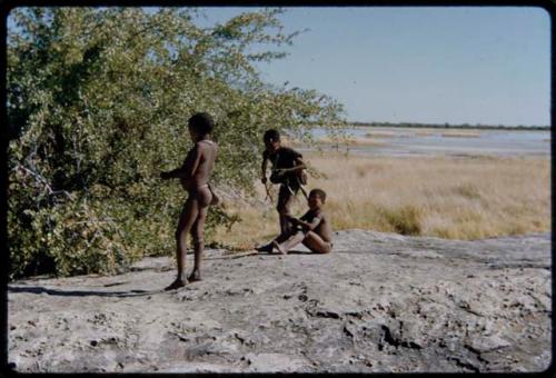 Children, Socialization--hunting, carrying: Three boys at a waterhole, with a pan filled with water in the background